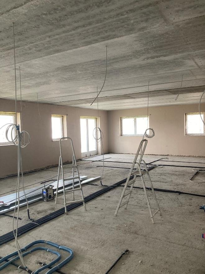 Verputzter Innenraum mit von der Decke hängenden Elektroleitungen, auf dem Boden verlegte Leerrohre und zwei Stehleitern